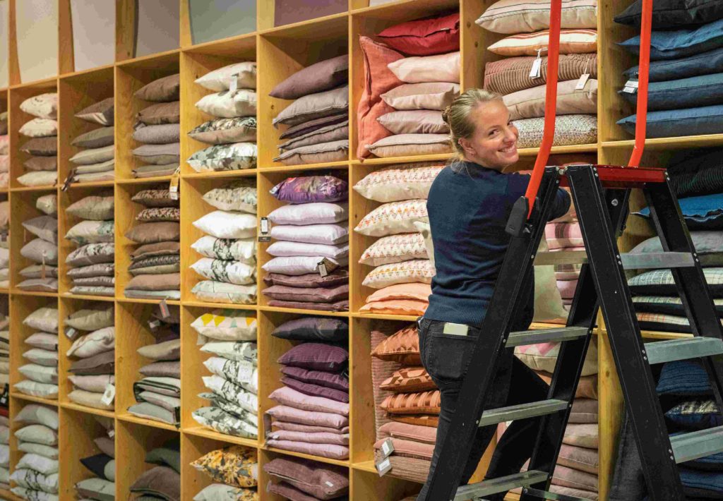 Meisje op ladder naast open kast gevuld met kussens
