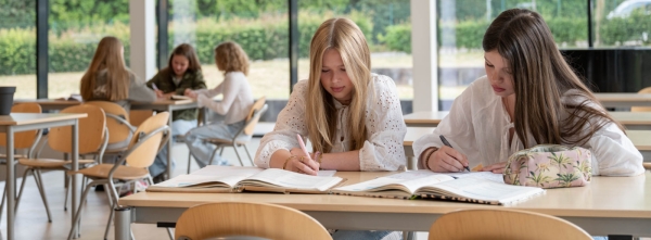 Huiswerkbegeleiding. Meisjes doen huiswerk in aula van school VO Gids 2026