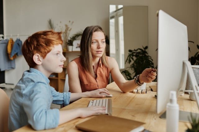 Vrouw wijst kind op informatie op beeldscherm in huiskamer | VO Gids 2026