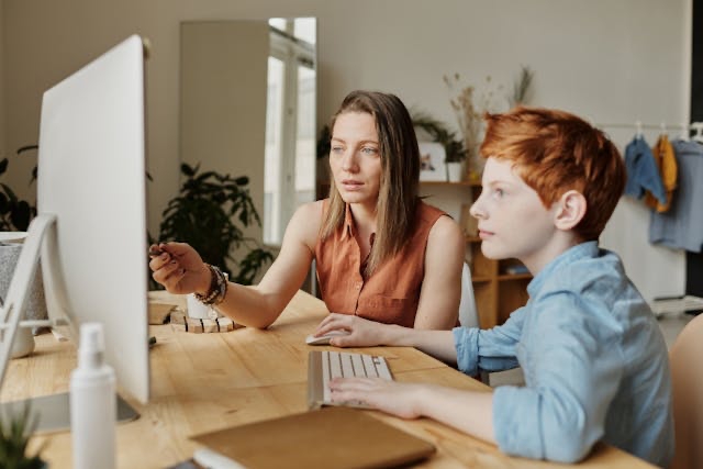Vrouw wijst kind op informatie op beeldscherm in huiskamer VO Gids 2026