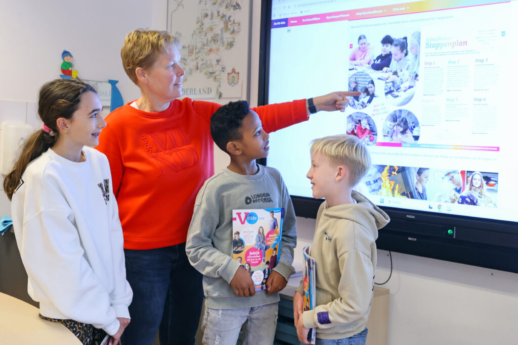 Juf wijst 3 leerlingen op VO Gids op digibord