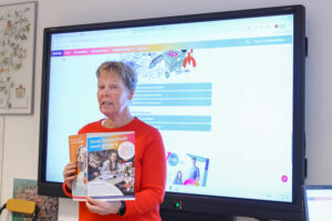 Juf met VO Gids in handen voor digibord legt uit over de VO Gids 2026