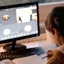 Kind kijkt in werkboek bij computerscherm | De VO Gids 2026