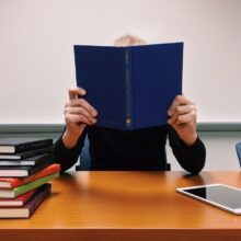 Persoon verschuilt zich achter blauw boek aan tafel | De VO Gids 2026