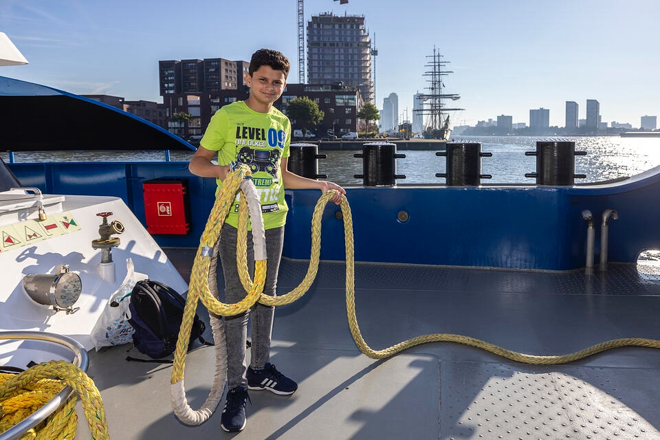 Jongen staat met jabel in handen op schip in havengebied | De VO Gids 2026