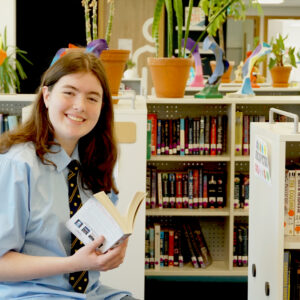 Charlotte staat met boek in haar handen voor boekenkast | De VO Gids 2027