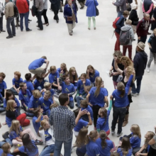 Groep kinderen in blauwe shirts zitten op grond tussen andere bezoekers | De VO Gids 2027