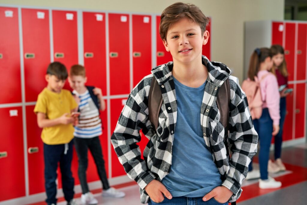 Leerlingen staan voor rode kluisjes op school met jongen in geruite bloes vooraan | De VO Gids 2027