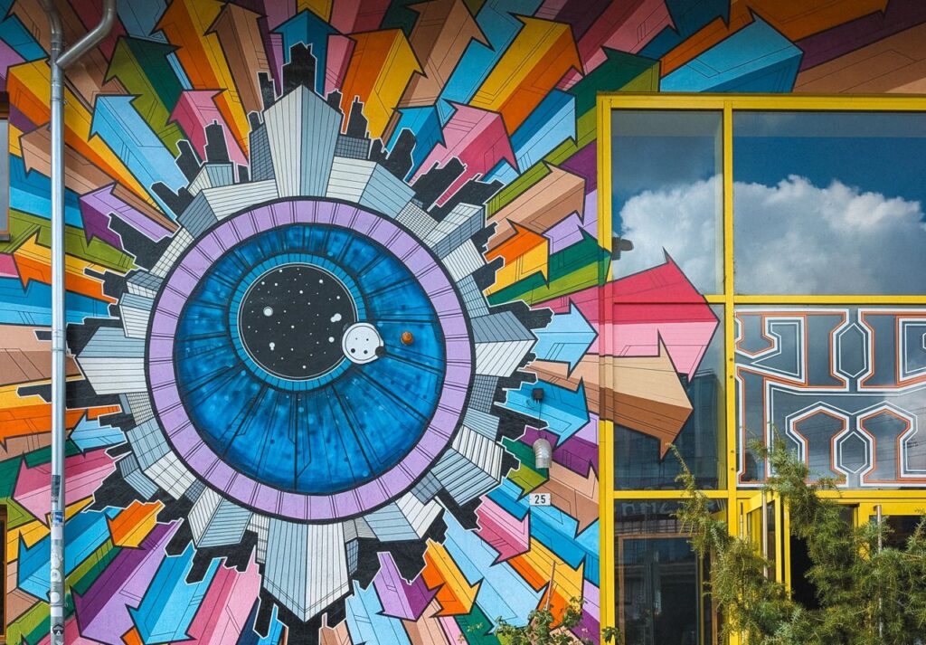 Buitenmuur en deel van raam beschilderd met pijlen in veel kleuren vanuit groot blauw oog | De VO Gids 2027