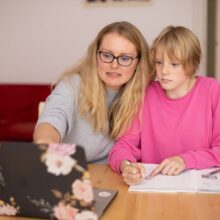 Vrouw wijst iets aan op een laptopscherm voor meisje in roze trui naast haar 